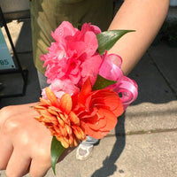 Close-up of a wrist with a colorful floral corsage on a concrete surface.