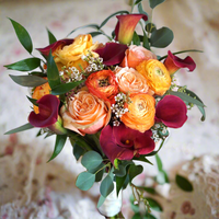 A bouquet of peach and orange flowers including roses and other foliage, arranged in a clear glass vase.