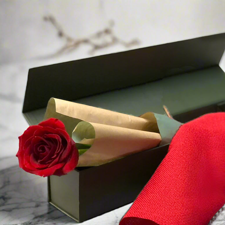 Red rose in a black box with gold paper on a light gray background